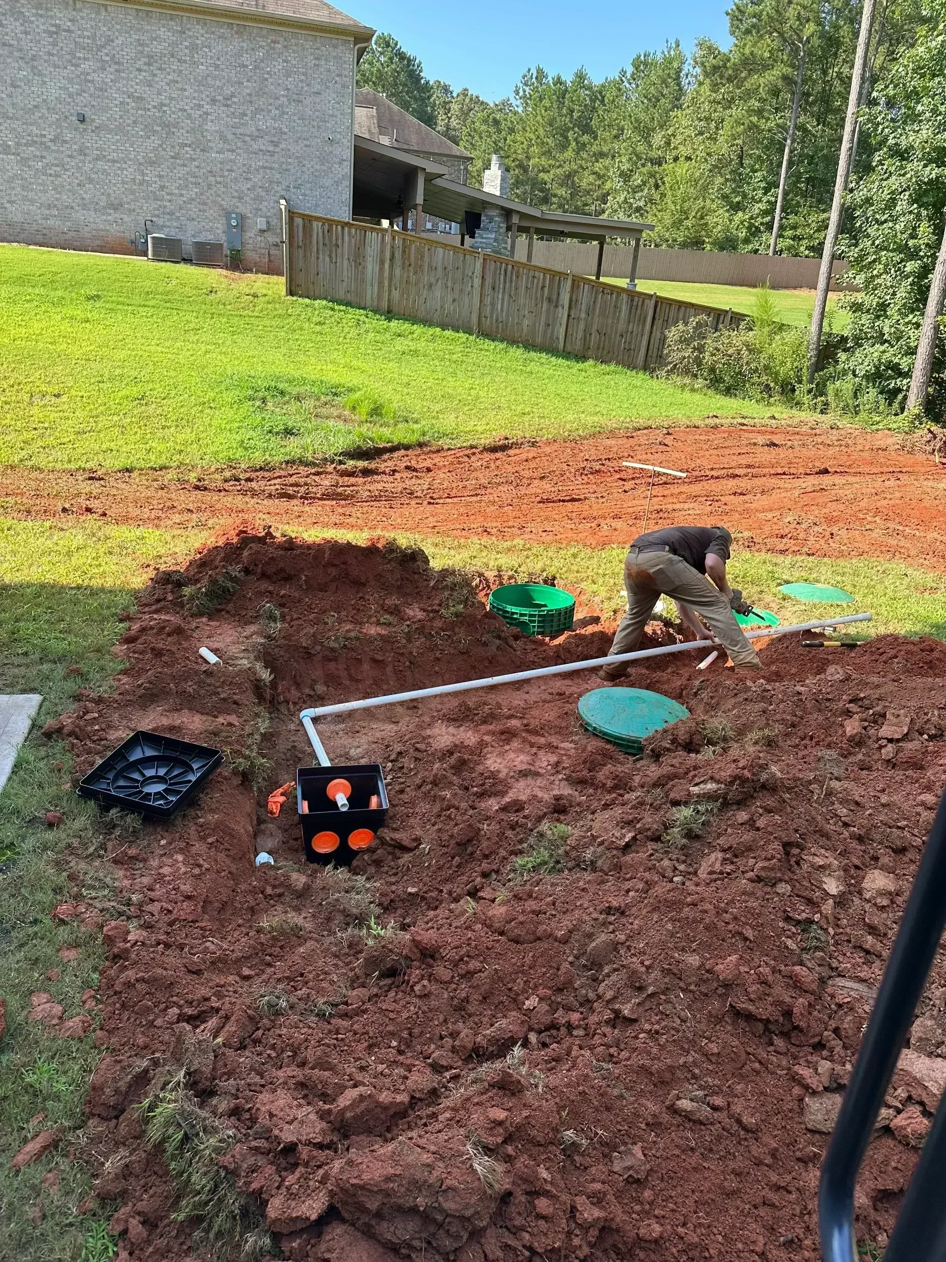 Septic system installation with drain field excavation, PVC piping, and distribution boxes in red clay soil