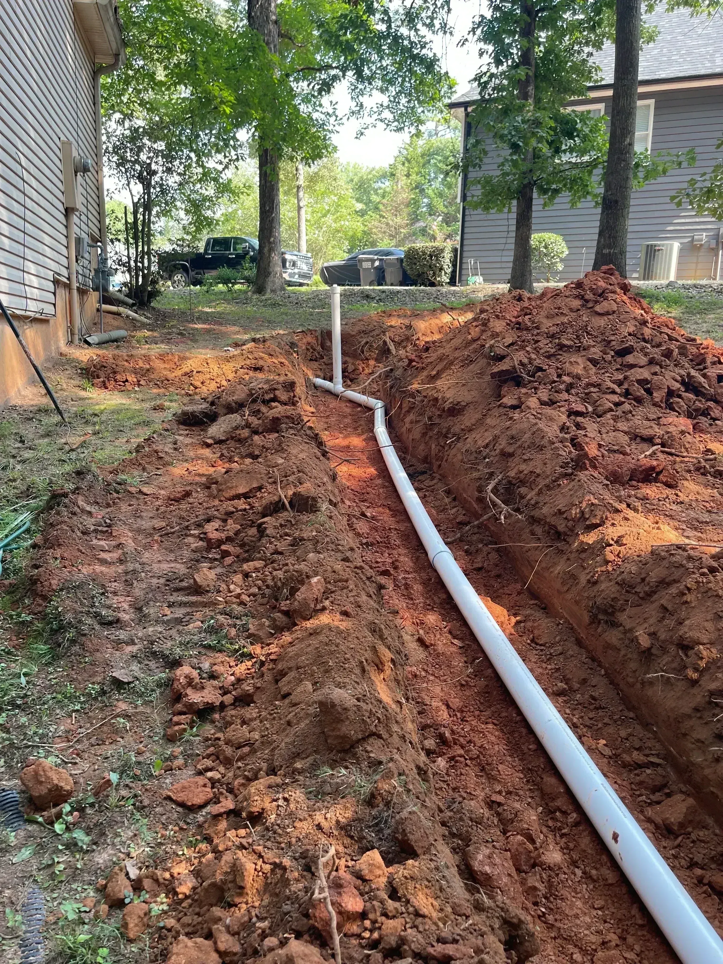 White PVC septic drainage pipe installed in excavated trench with proper slope and grade