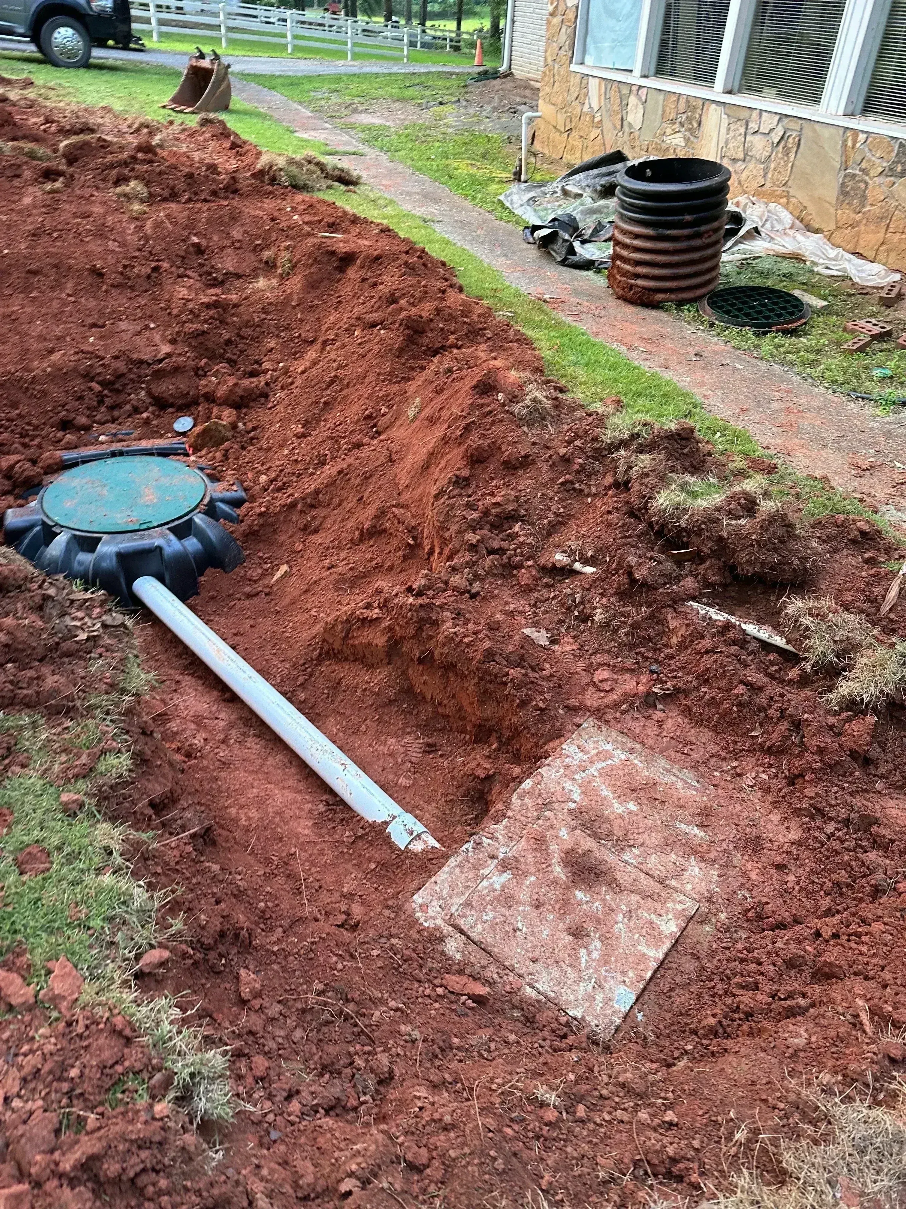 Septic system installation with PVC piping, access ports, and drain field excavation in red clay soil