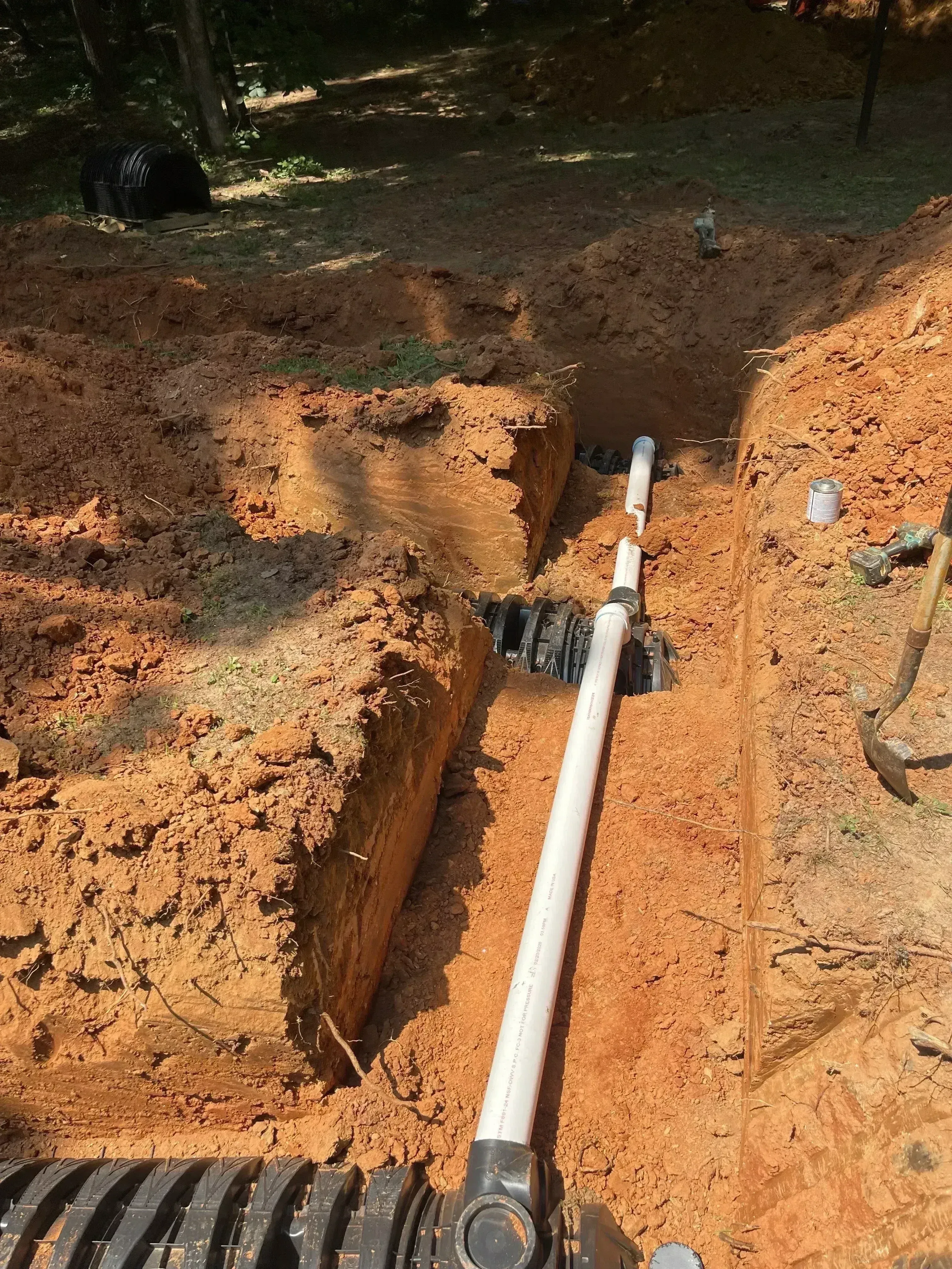 White PVC septic pipe installed in excavated trench with black couplings and proper grading