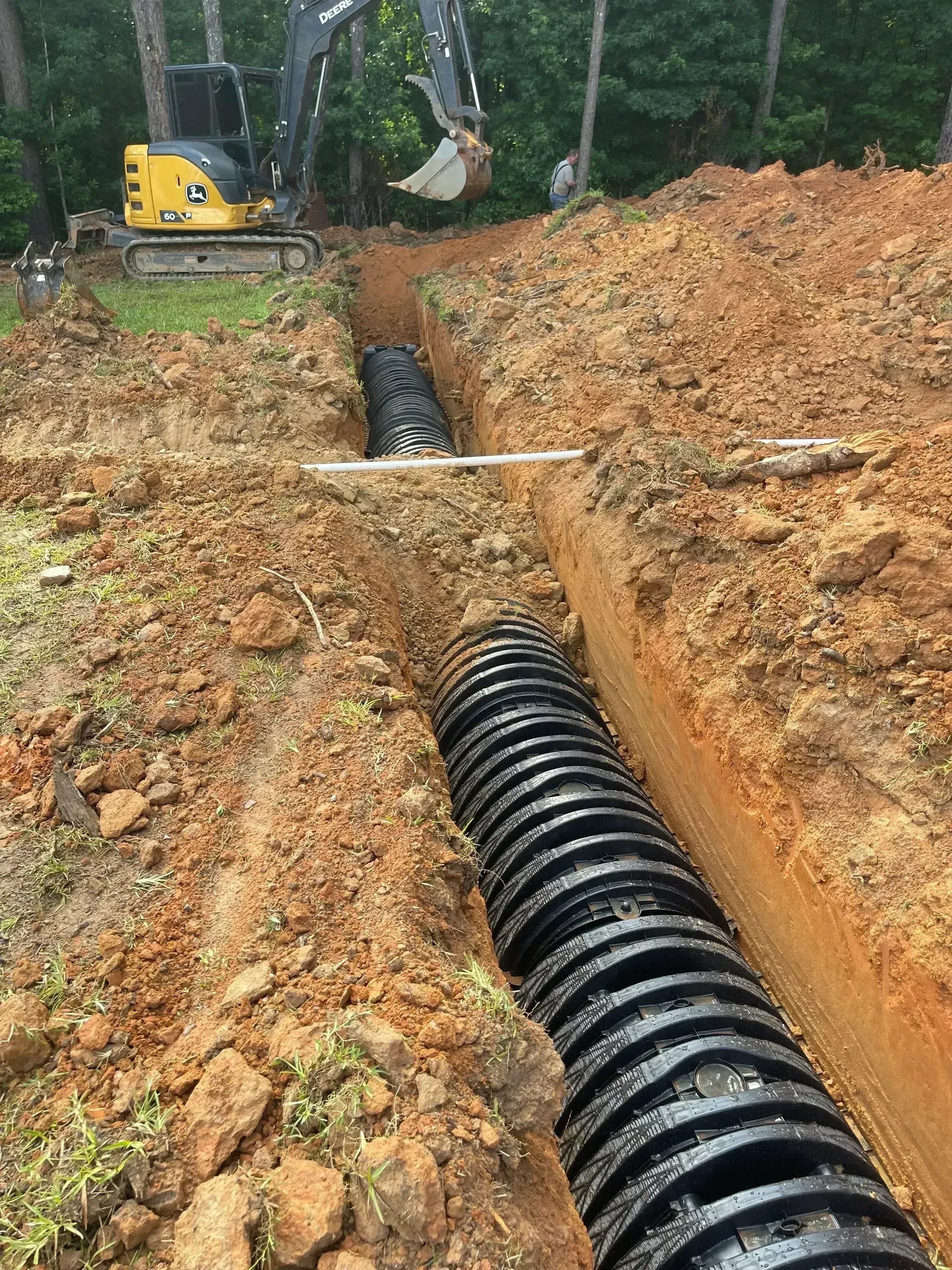 Corrugated black drainage pipes installed in excavated trench with compacted soil backfill