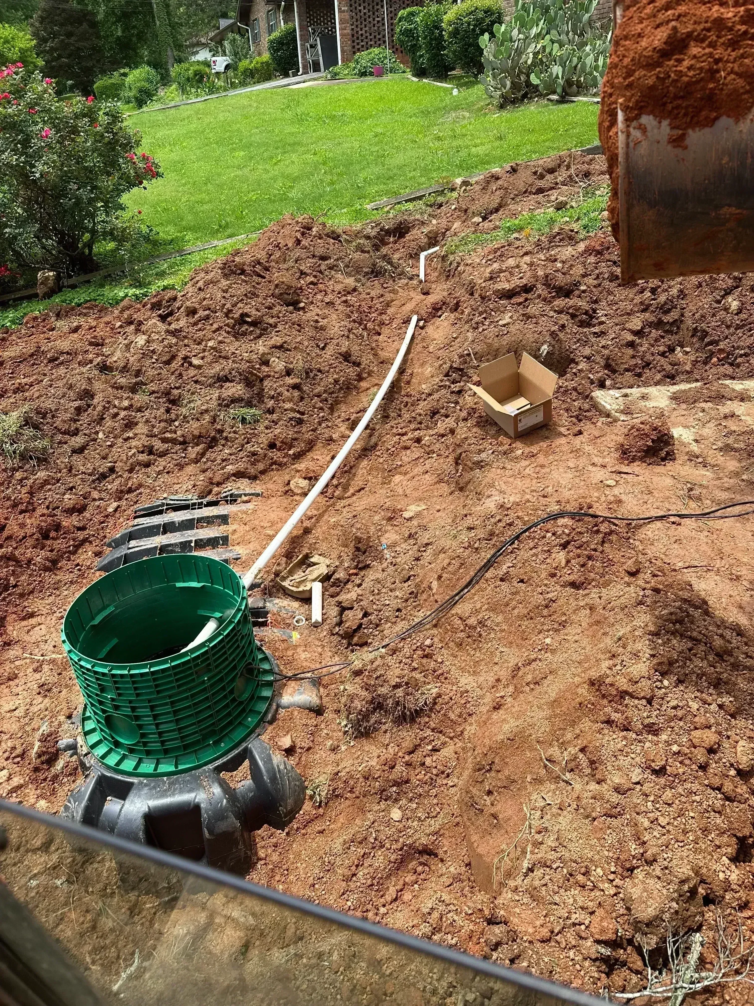 Green septic tank installed in excavated pit with PVC drainage lines and access covers