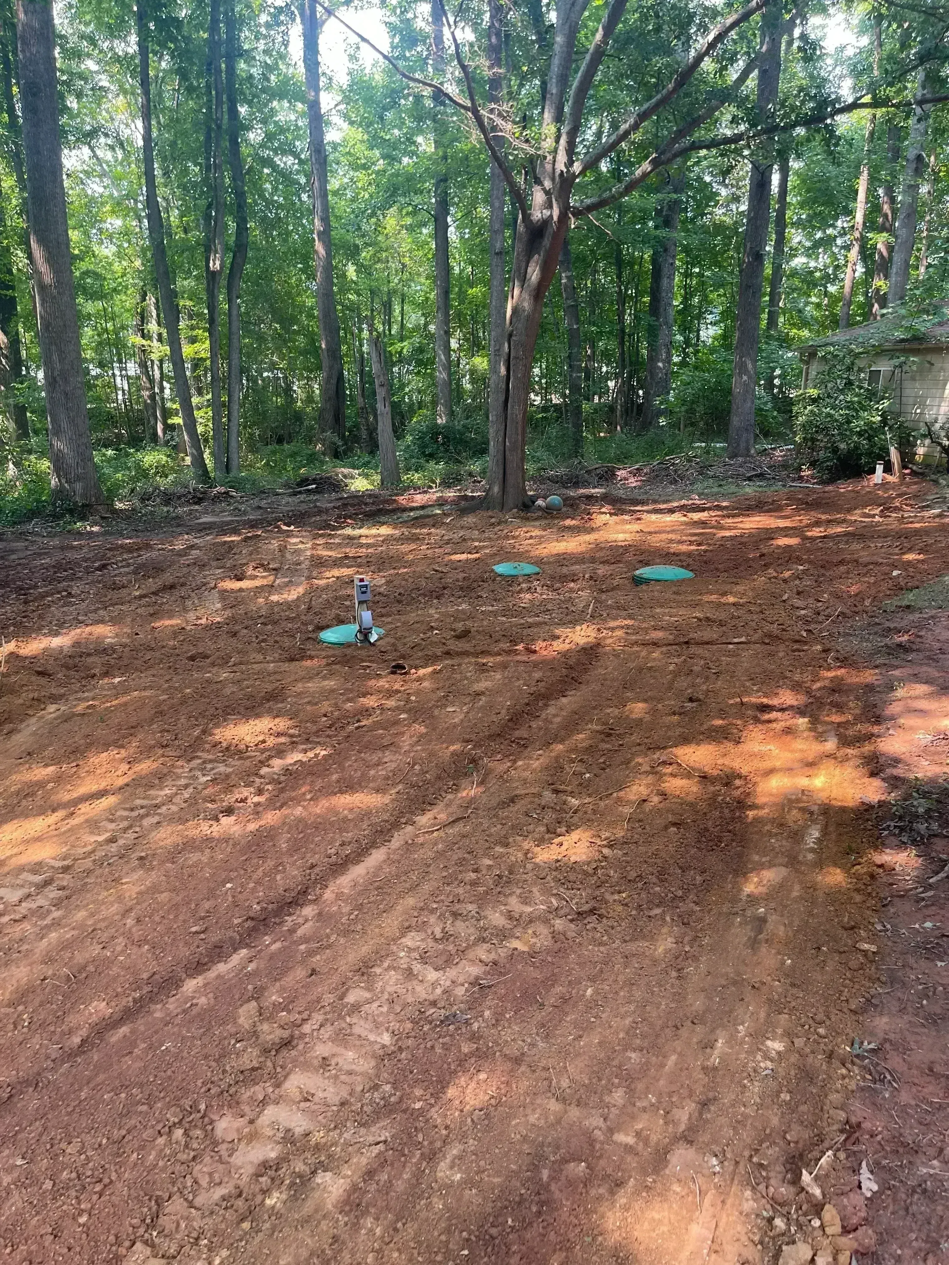 Excavated septic drain field with blue-marked distribution lines in reddish soil