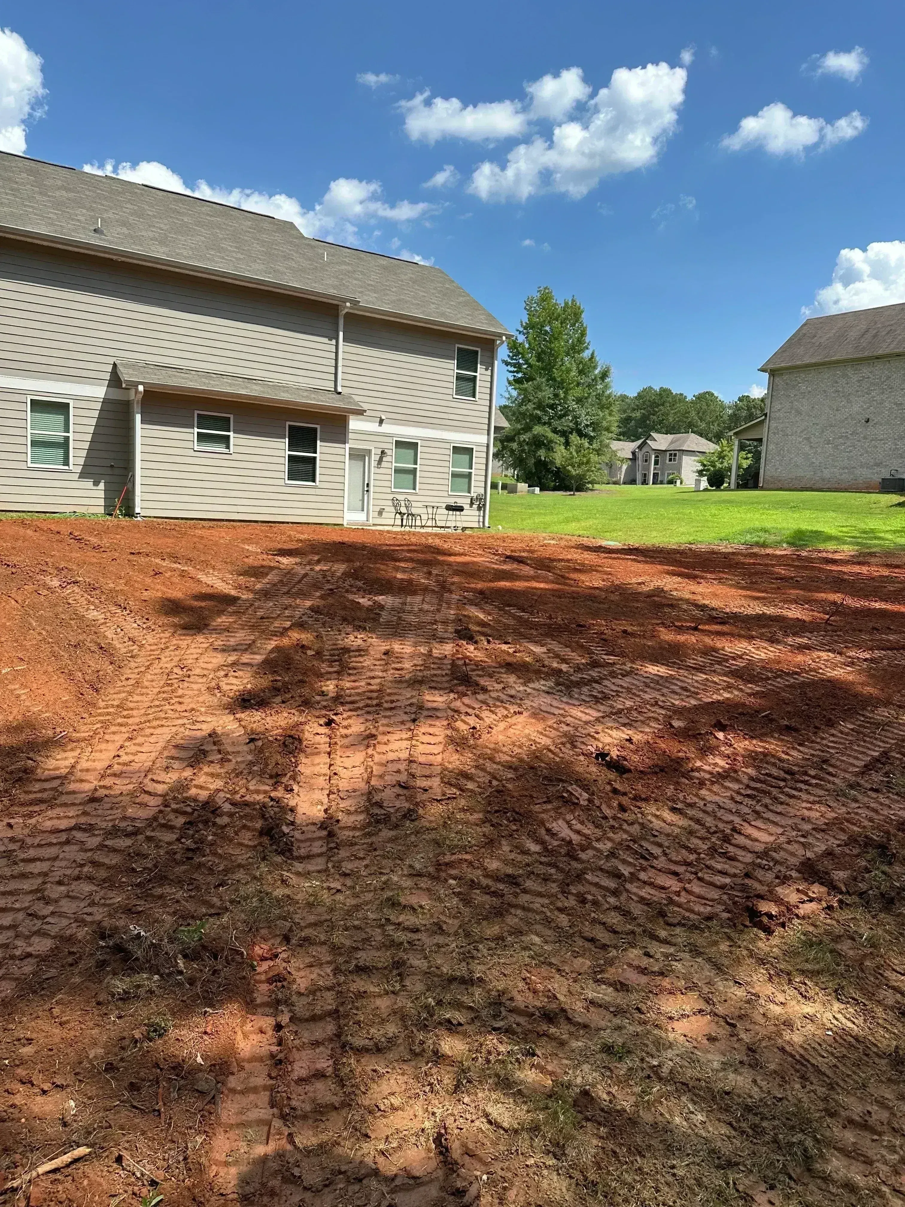 Excavated septic drain field with red clay soil, metal-sided residential building, and manicured lawn