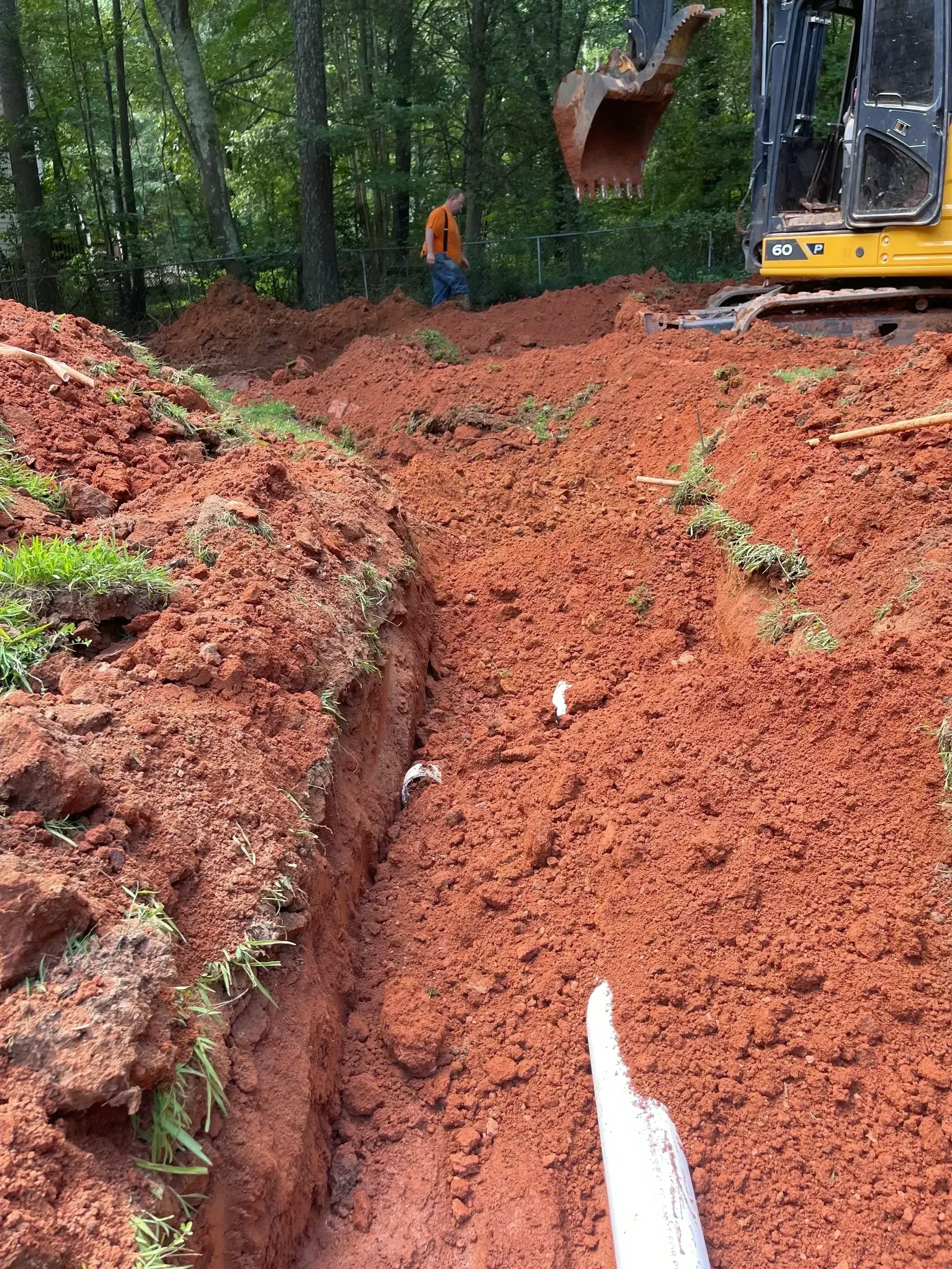 Red clay soil excavation trench for septic system installation with equipment and site preparation