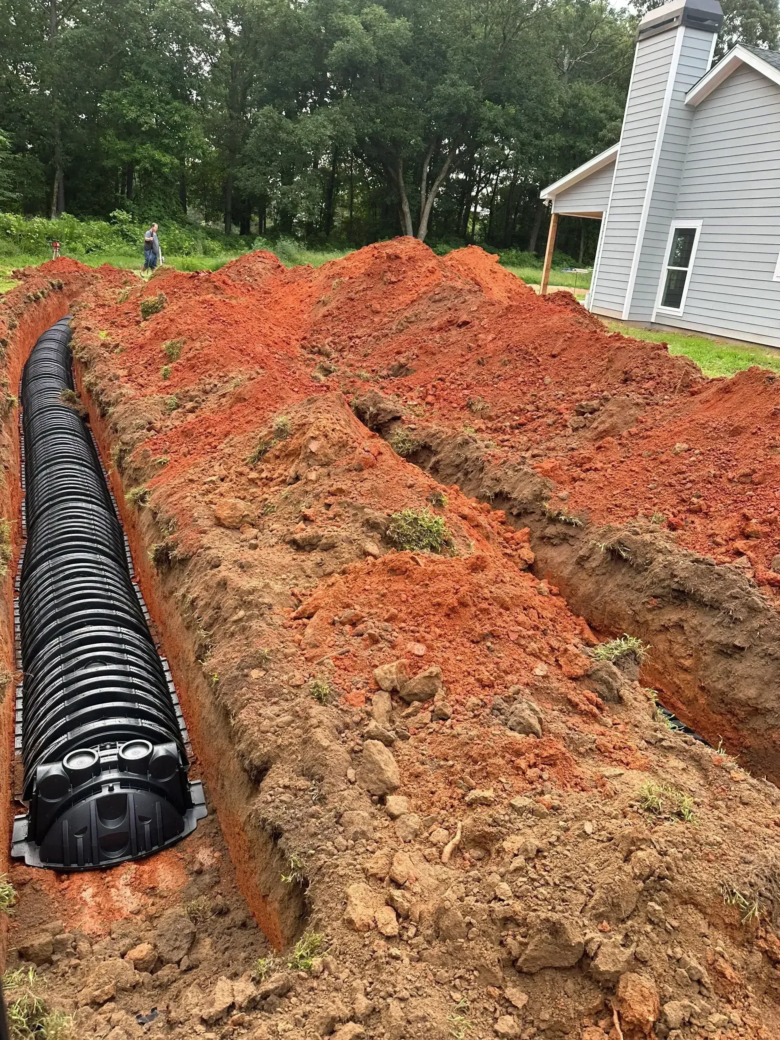 Corrugated plastic septic tank installed in excavated red clay soil with metal structure visible in background