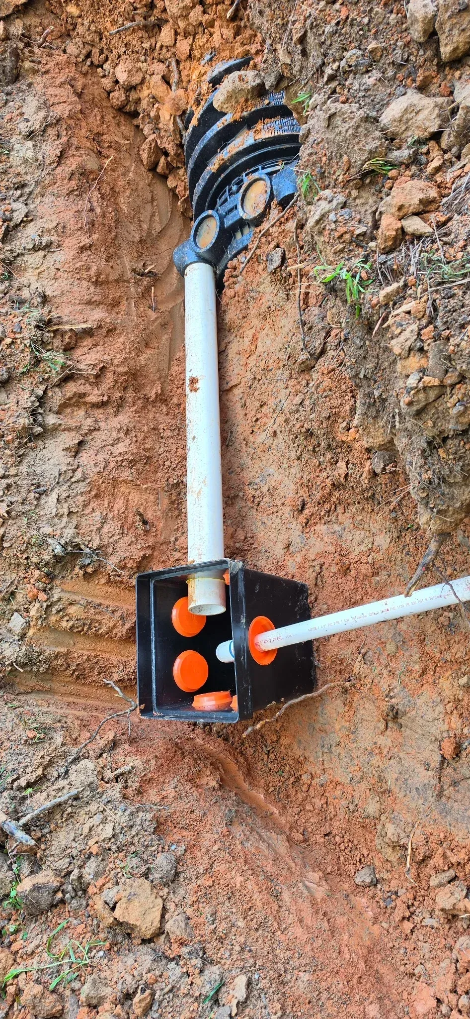 Septic distribution box with PVC piping and orange ports installed in excavated trench