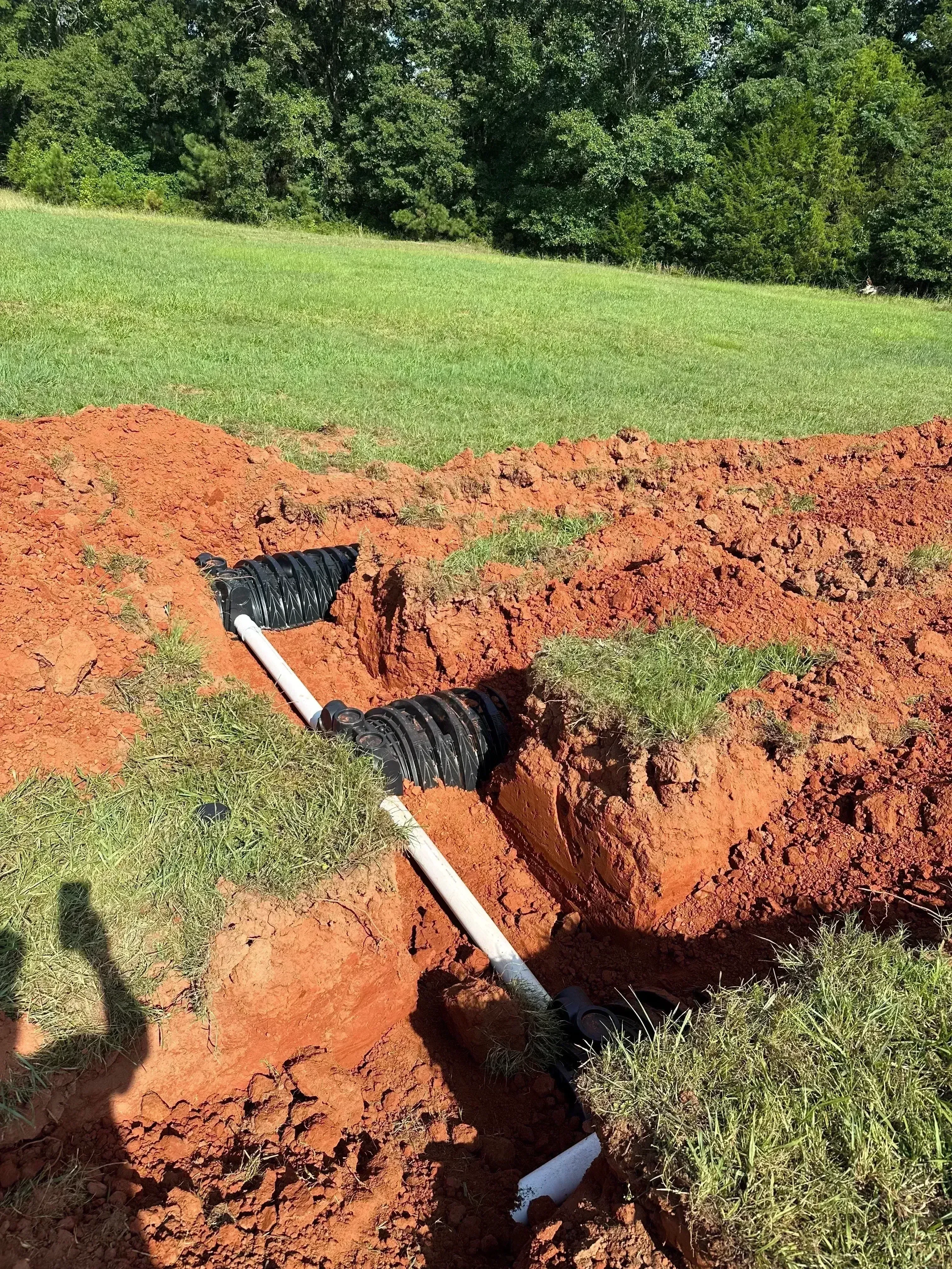 Dual black corrugated septic drain lines with PVC connectors in red clay trench excavation
