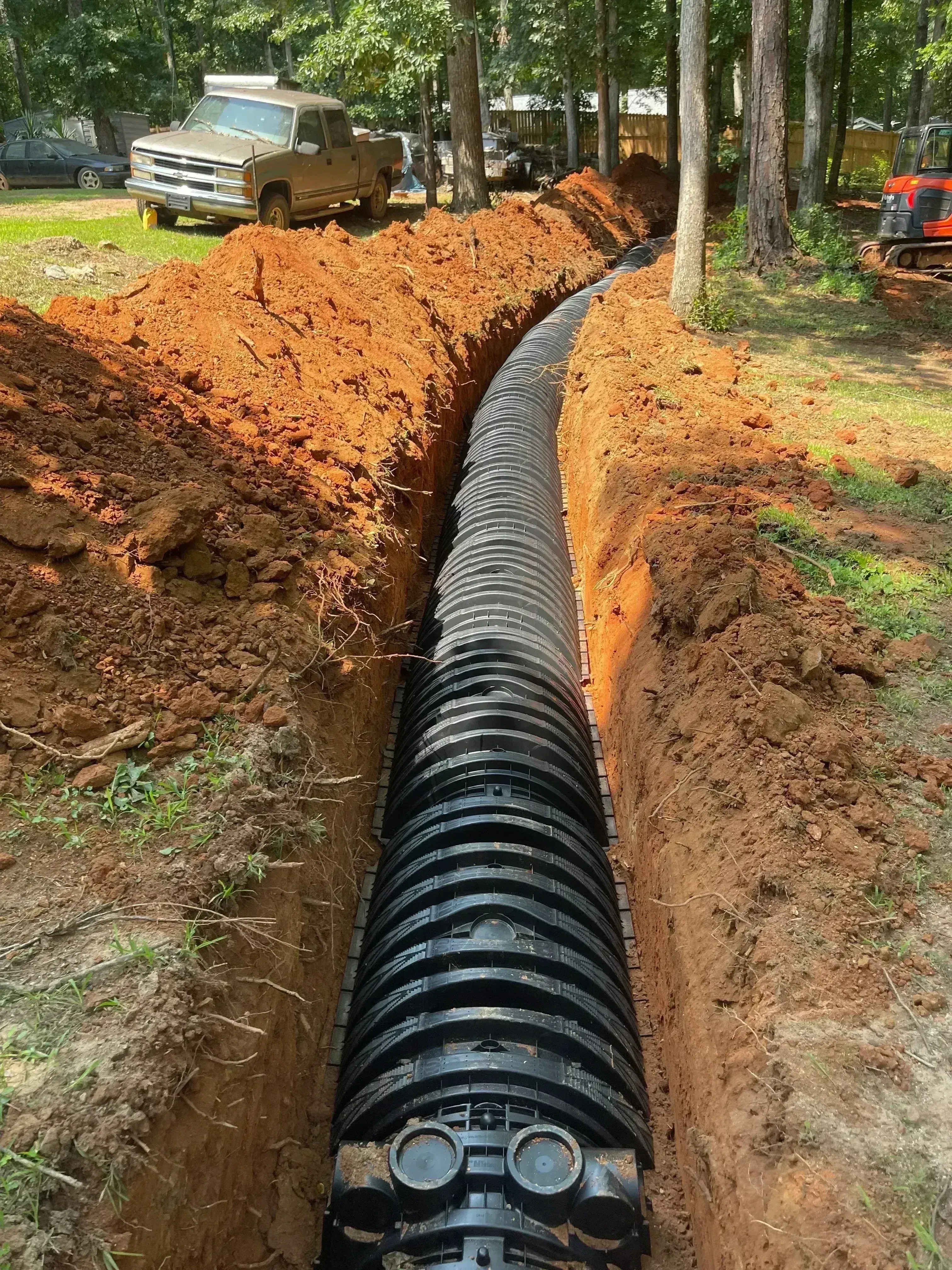Corrugated plastic septic tank installed in excavated trench with red clay soil