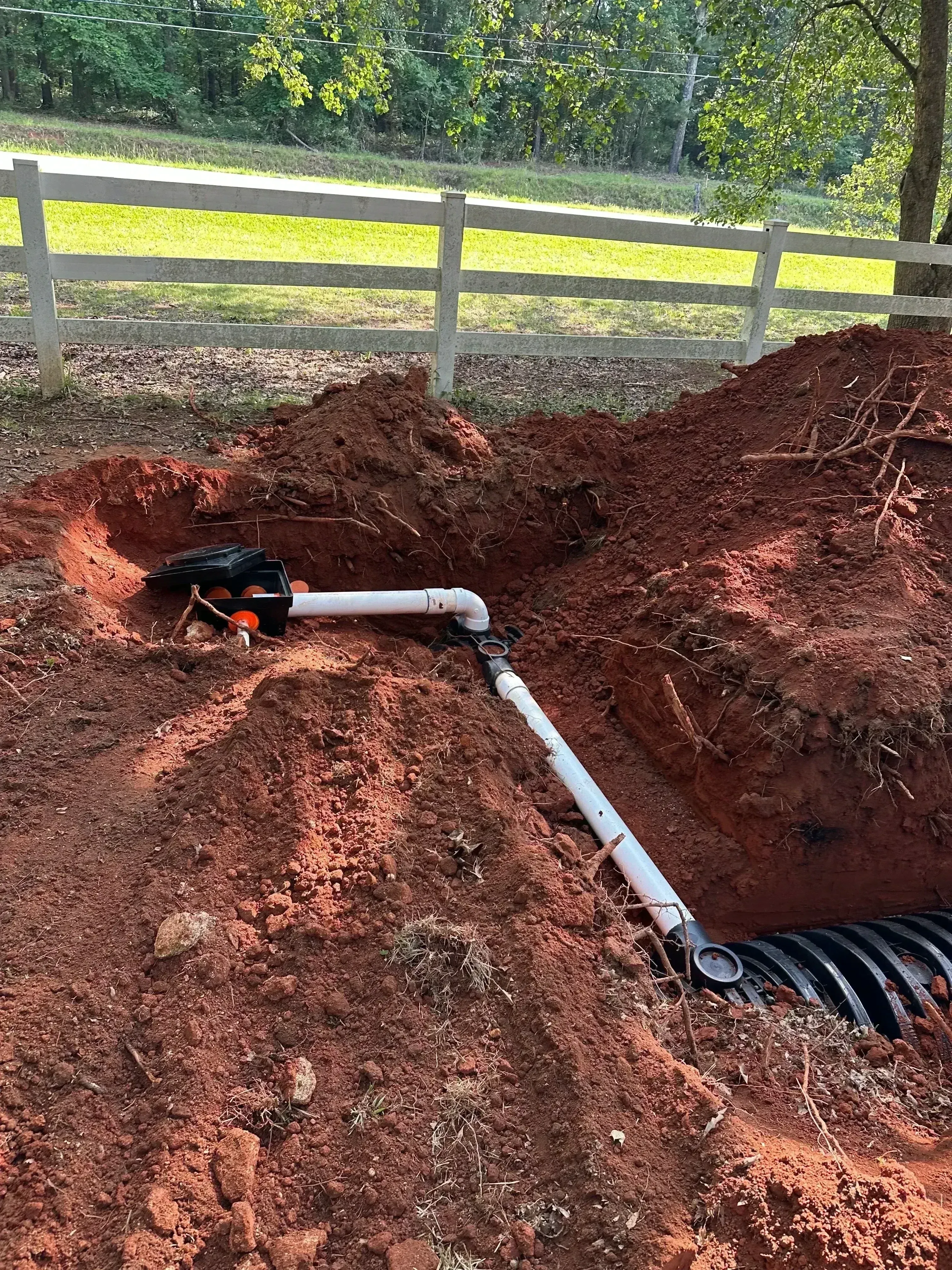 White PVC septic piping with black valves installed in red clay excavation trench