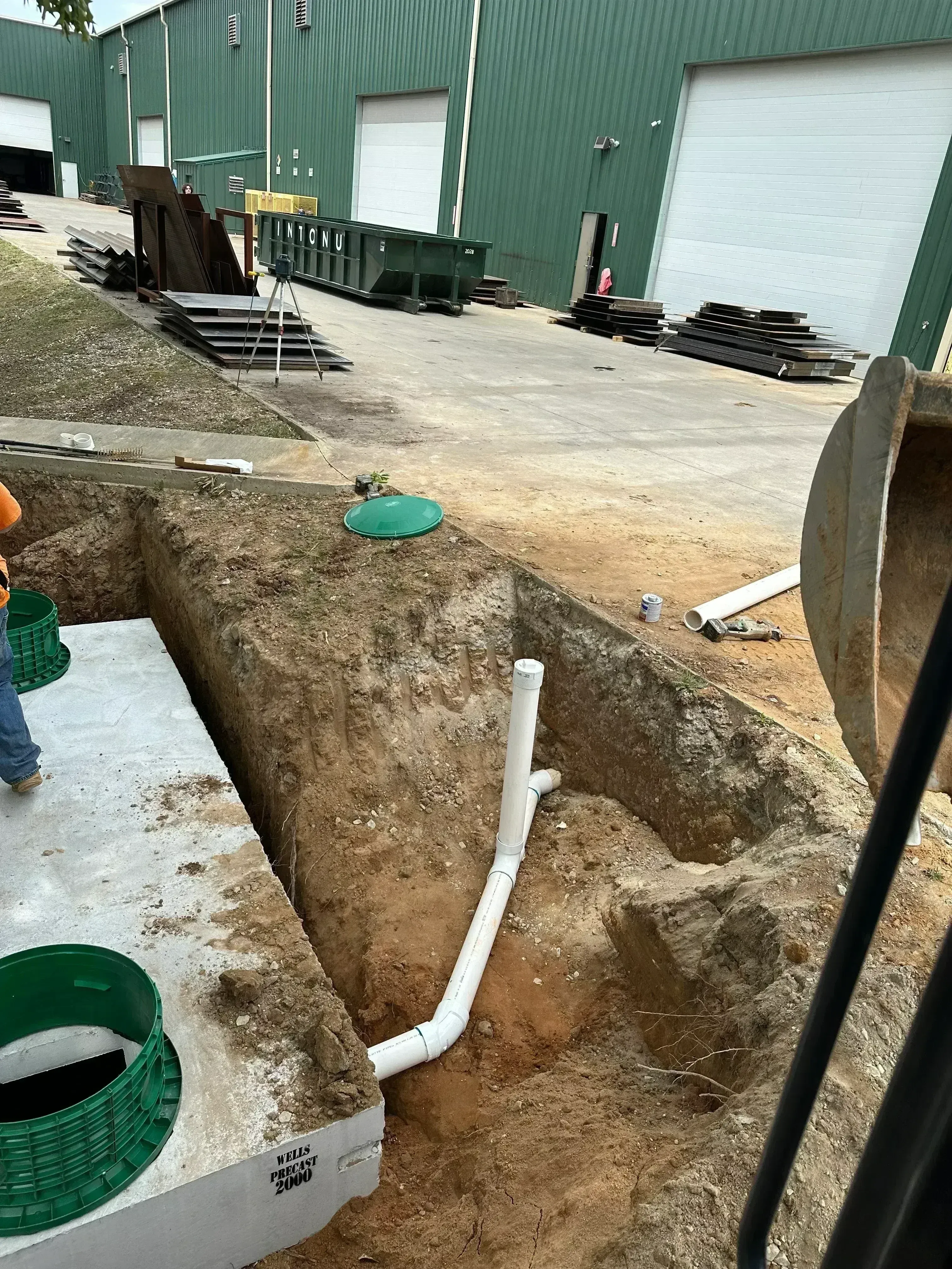 Septic tank with green covers and white PVC drainage pipes in excavated drainage field
