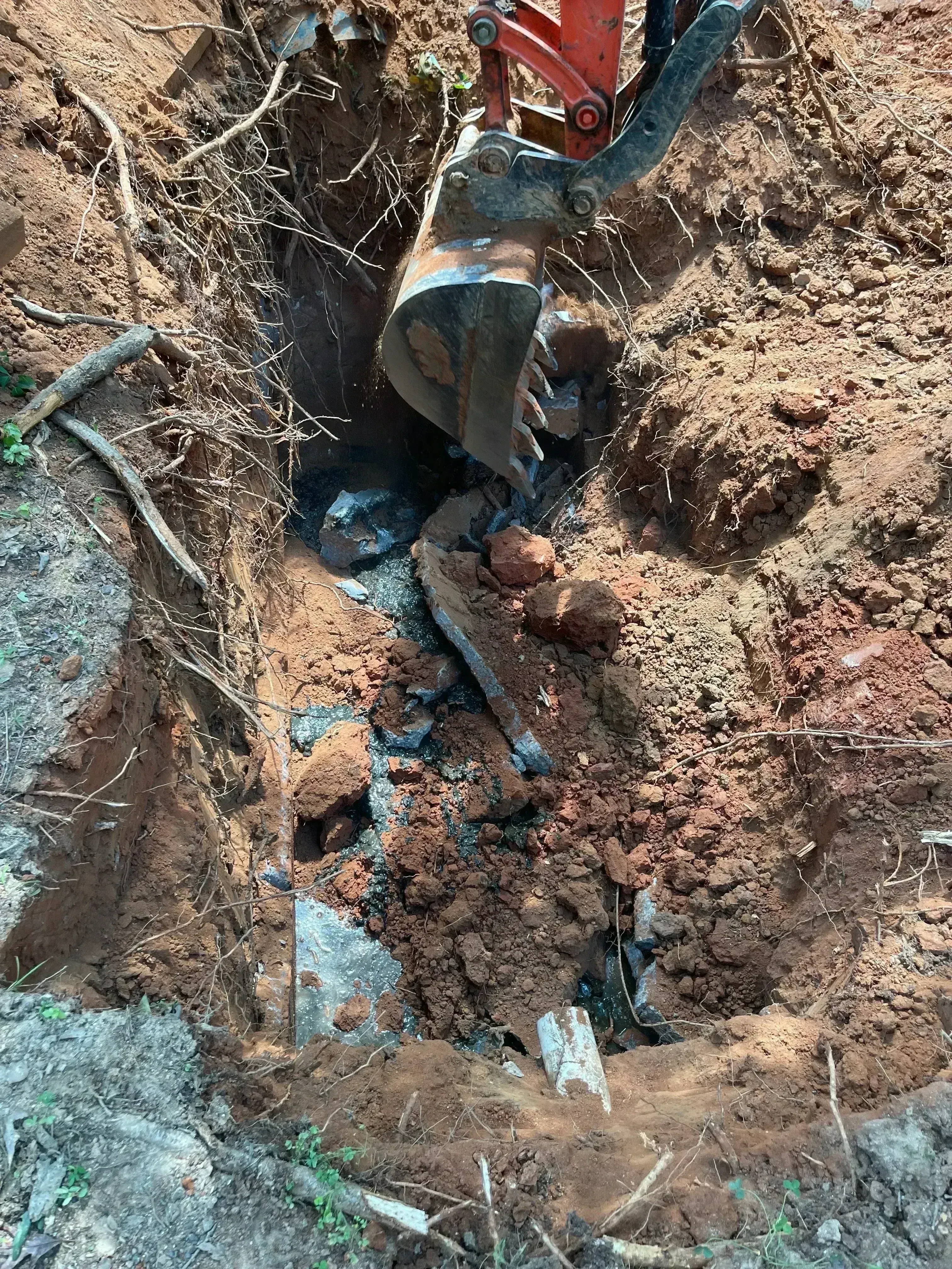 Excavated septic tank with blue PVC pipes and concrete sections visible in soil